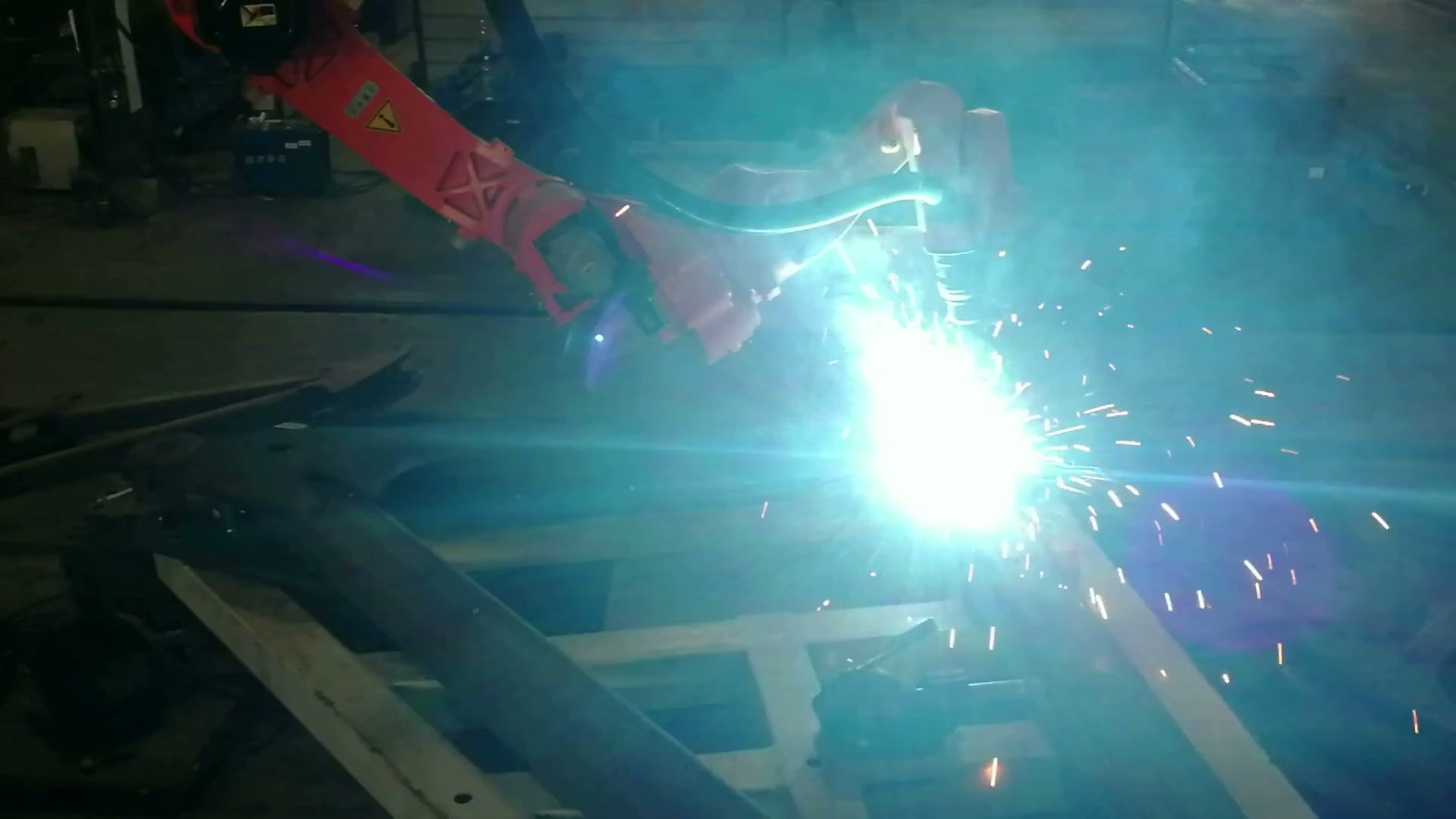 A bright welding arc is visible at one joint on the fixed large frame.