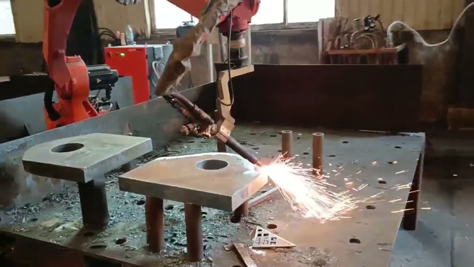 Flame cutting torch held by a robot at the edge of a thick steel plate with sparks streaming down and out