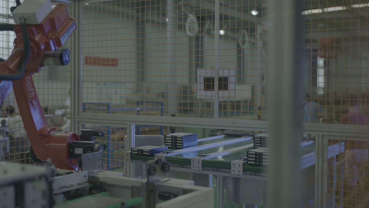 The six-axis robot inside its safety fence, with the conveyor line and the shop floor around it