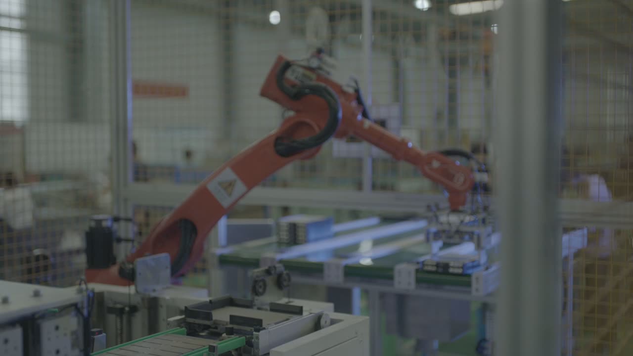 The arm reaches toward the row of dark rectangular modules on the green belt conveyor