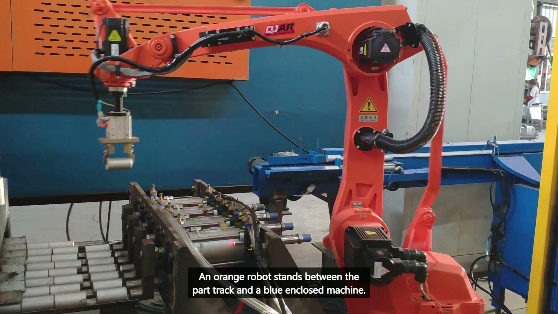 The downward parallel gripper holds one short cylindrical part above the roller-track area.