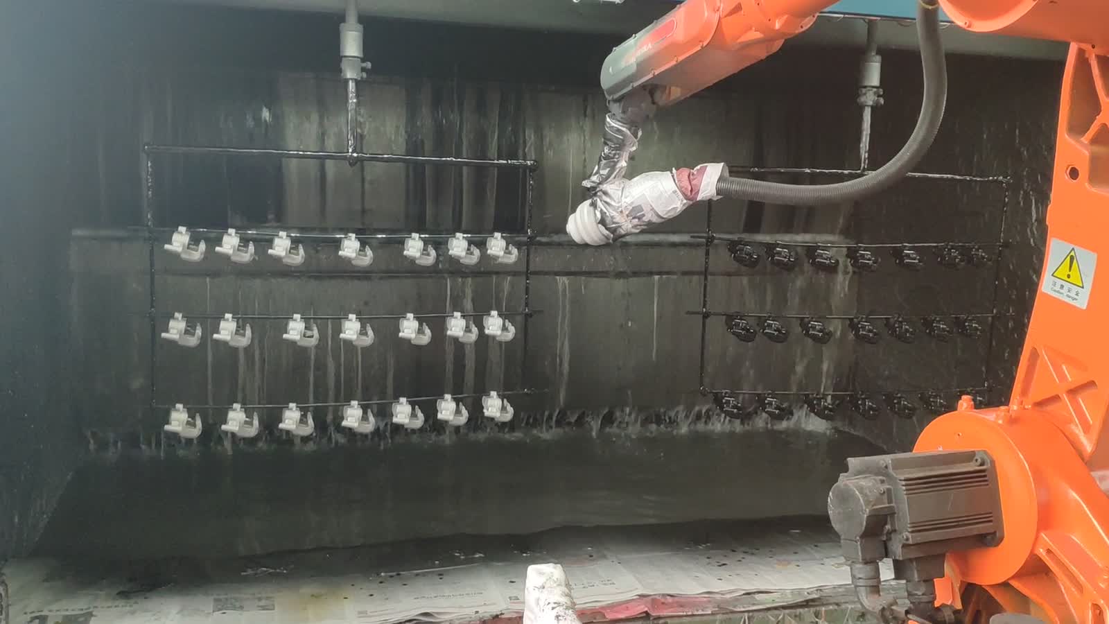 A robot with a spray gun in a paint booth full of hanging parts