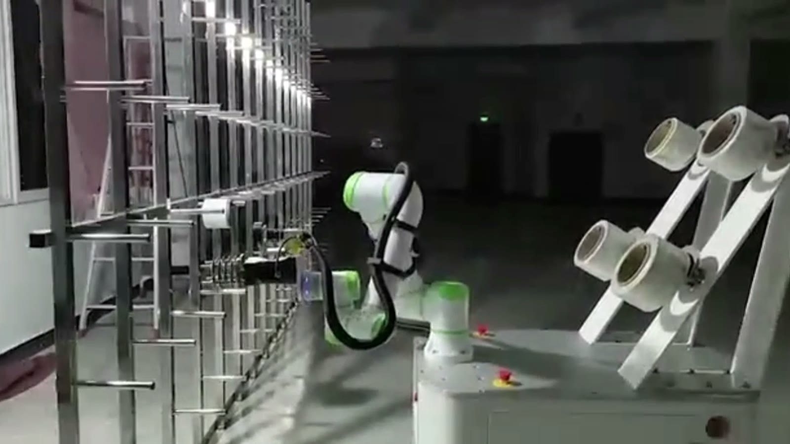 White cobot with green joints on a mobile base, with an angled rack of white yarn bobbins on one side and a multi-level creel on the other