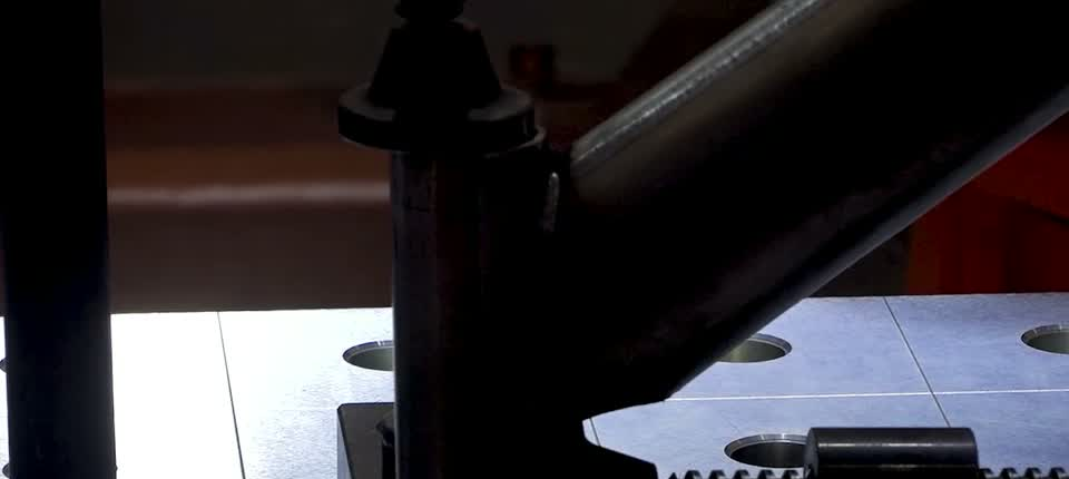 Close-up of an angled tubular frame joint held on a perforated fixture table