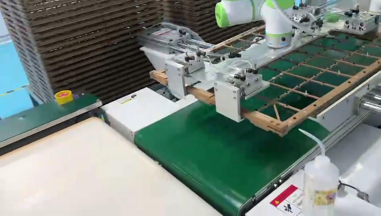 A robot supplies a grid carrier frame at the green conveyor