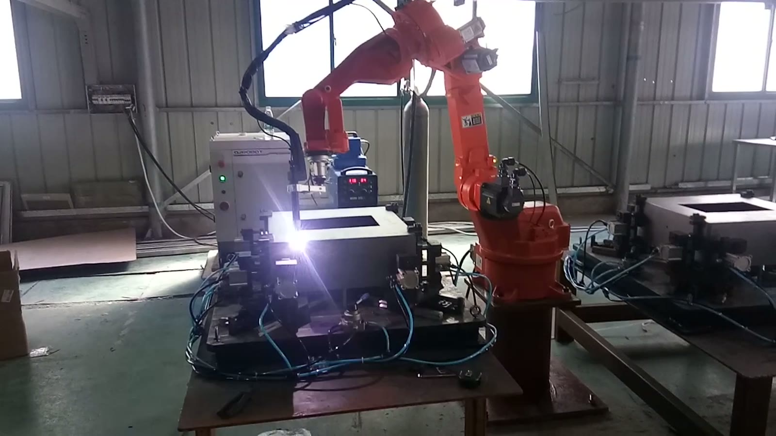 Welding torch striking an arc at the top edge of a square sheet-metal box held in a fixture