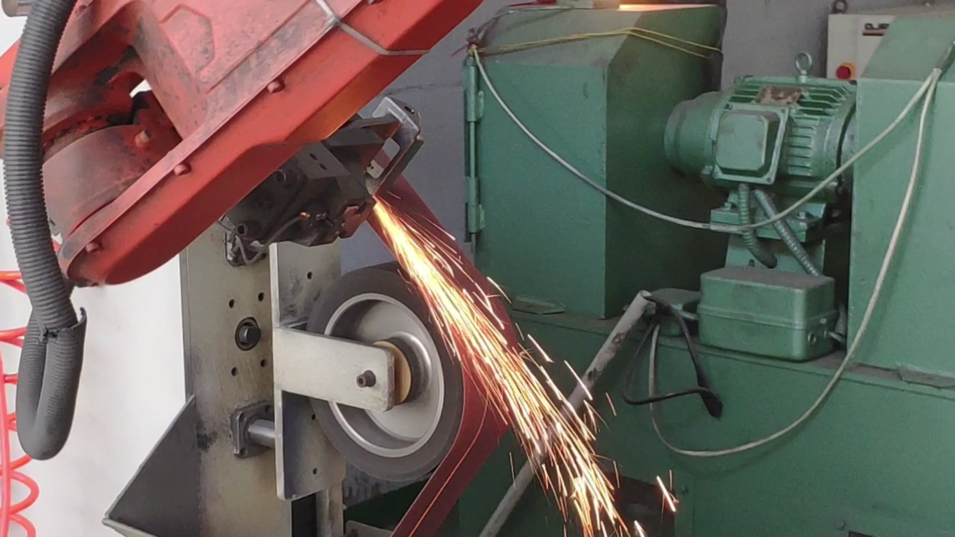 A robot gripper presses a door hinge against the running belt, sparks marking the contact point