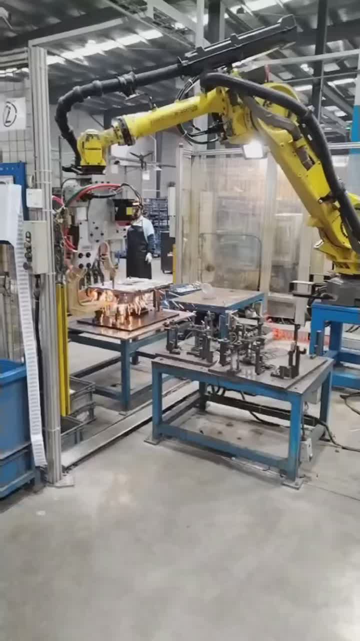 Visible spark burst at the gun and fixture area during robotic spot welding