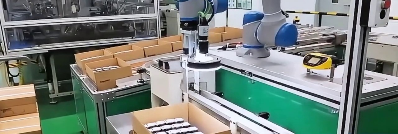 The robot tool is near the right-hand worktable, showing the relationship between the carton and the adjacent station.