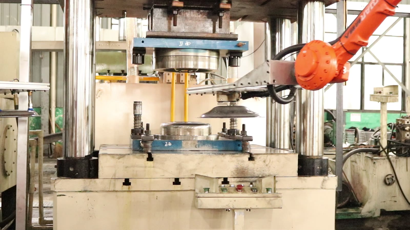 Robot with a flat forked gripper carrying a round steel blank over the lower die of a four-column hydraulic press