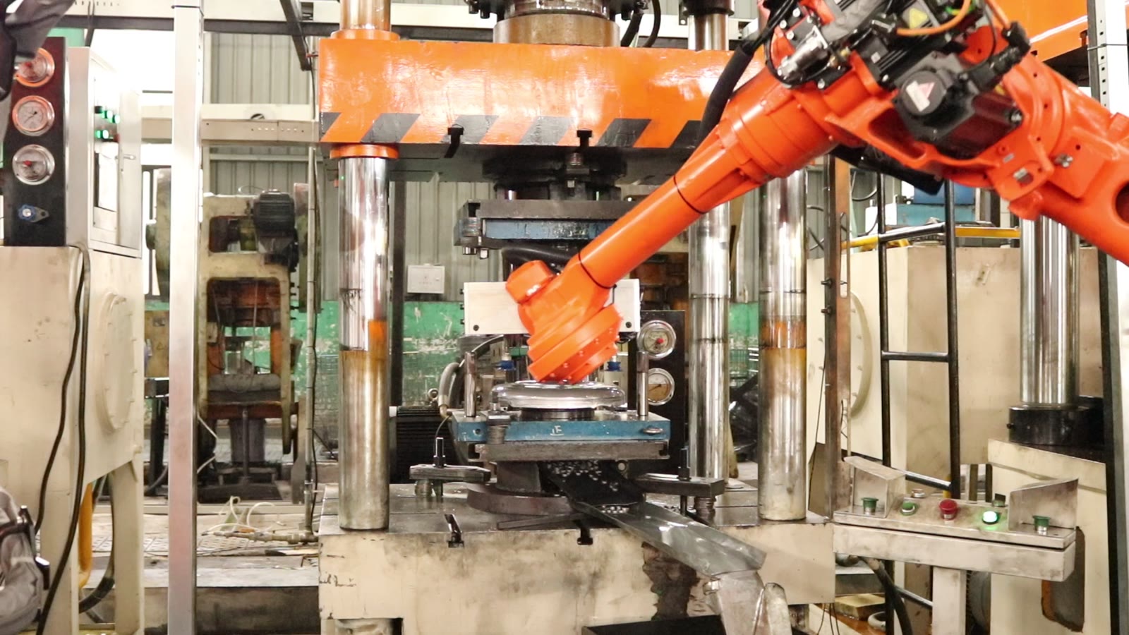 Orange six-axis robot arm reaching between the upper and lower die of a four-column hydraulic press
