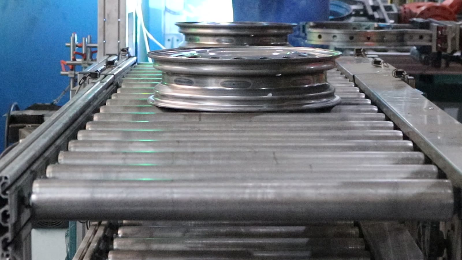 Rims with a row of holes travelling one after another along a roller conveyor
