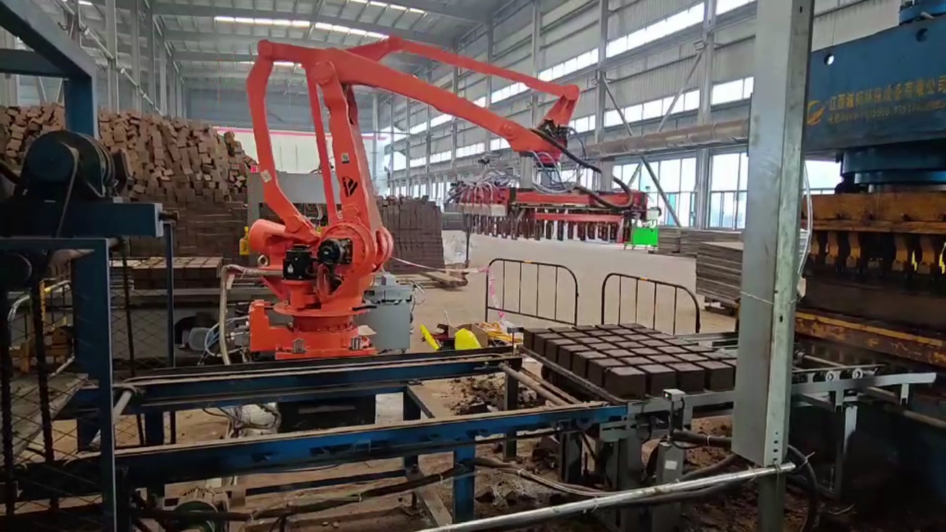 A four-axis palletizing robot lifts a row of blocks with a multi-clamp gripper beside the press