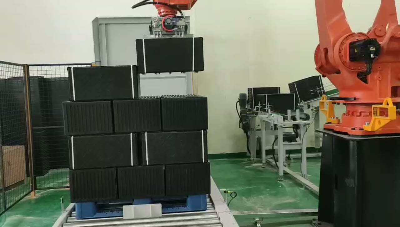 オレンジ色のパレット積みロボットが、積み重ねられた黒い苗トレイの束を持ち上げている。