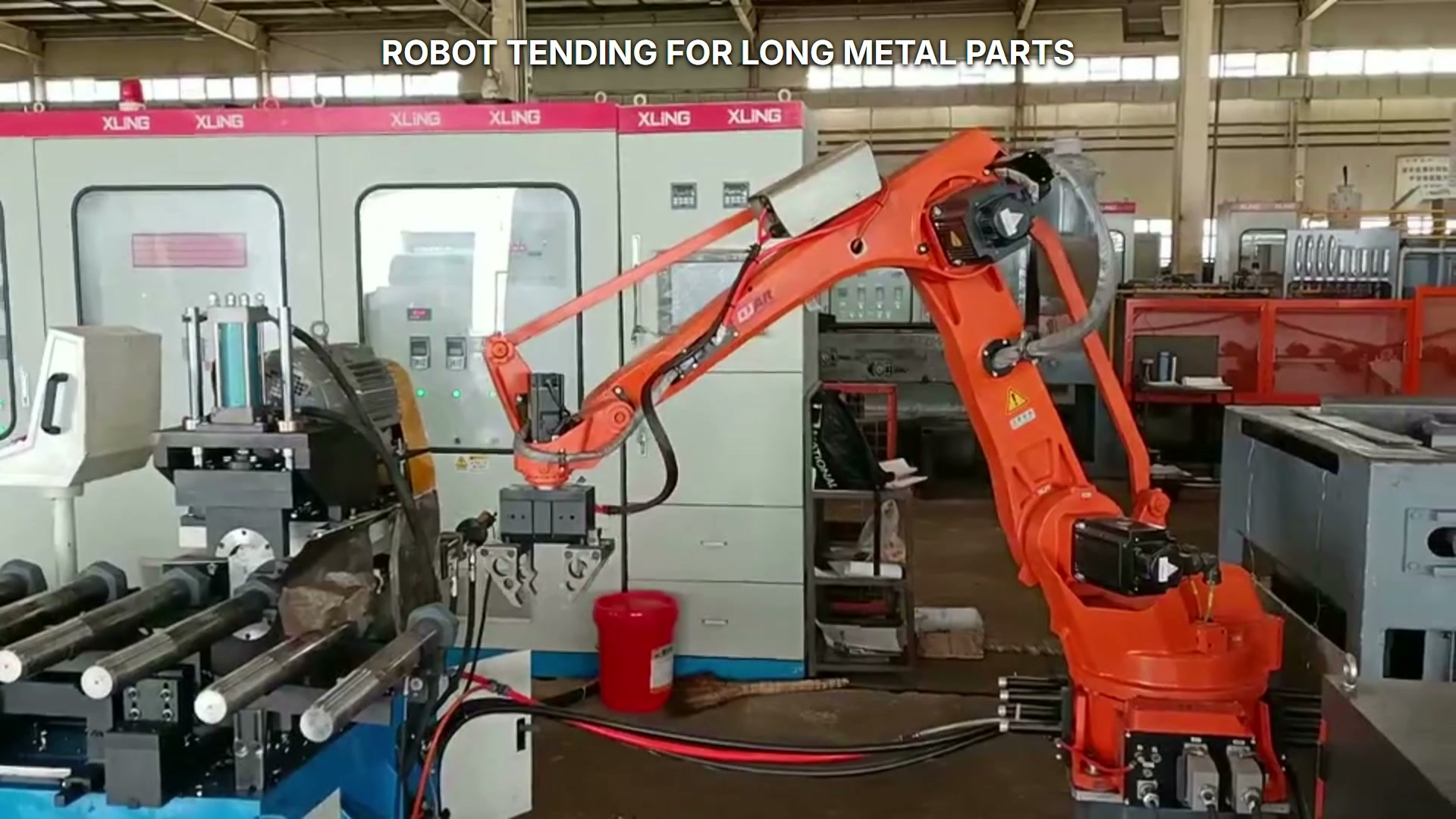 An orange industrial robot works between a left machine or holding station and a right roller-table station.