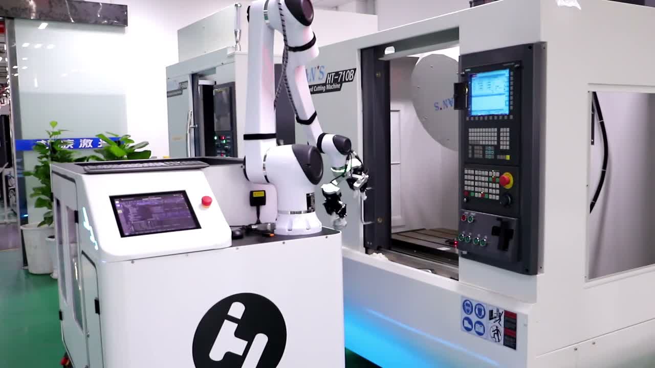 The arm and end effector are positioned at the CNC machine opening during the transfer sequence.
